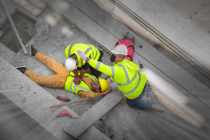 Two construction workers assisting an injured colleague lying on the ground, possibly performing CPR.