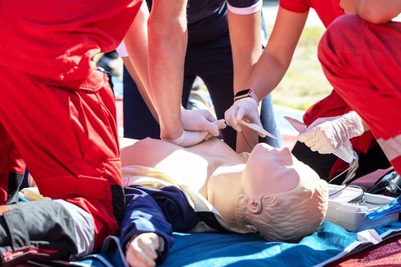 Three people practice CPR and use a defibrillator on a medical dummy.